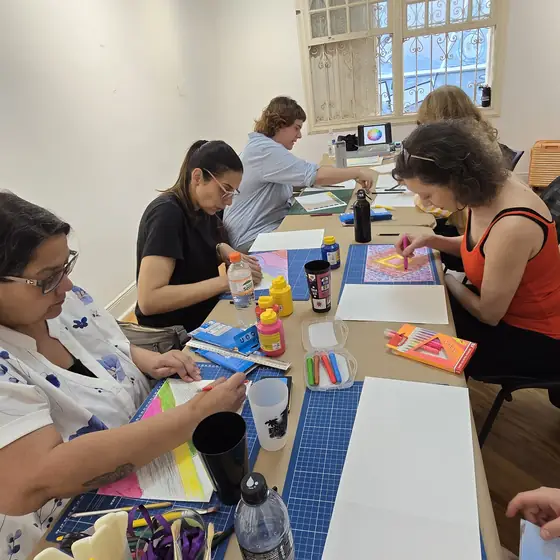Turma da oficina de encadernação trabalhando nas mesas, com papéis coloridos e tintas