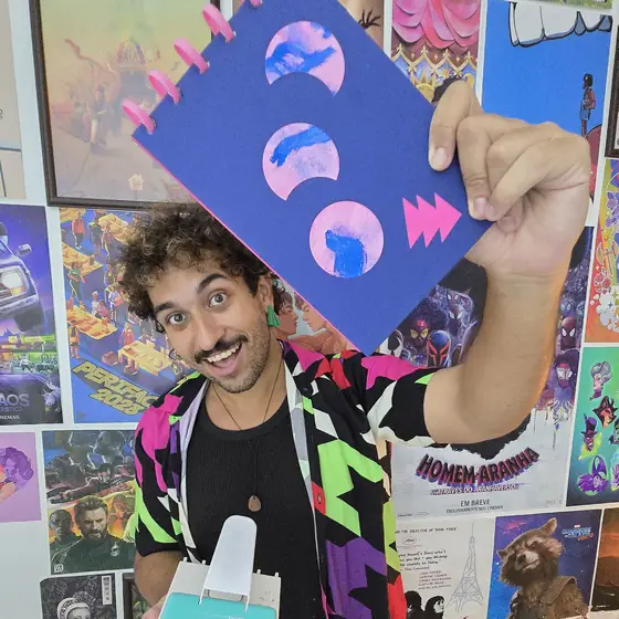 Sérgio sorrindo e segurando um sketchbook azul feito à mão